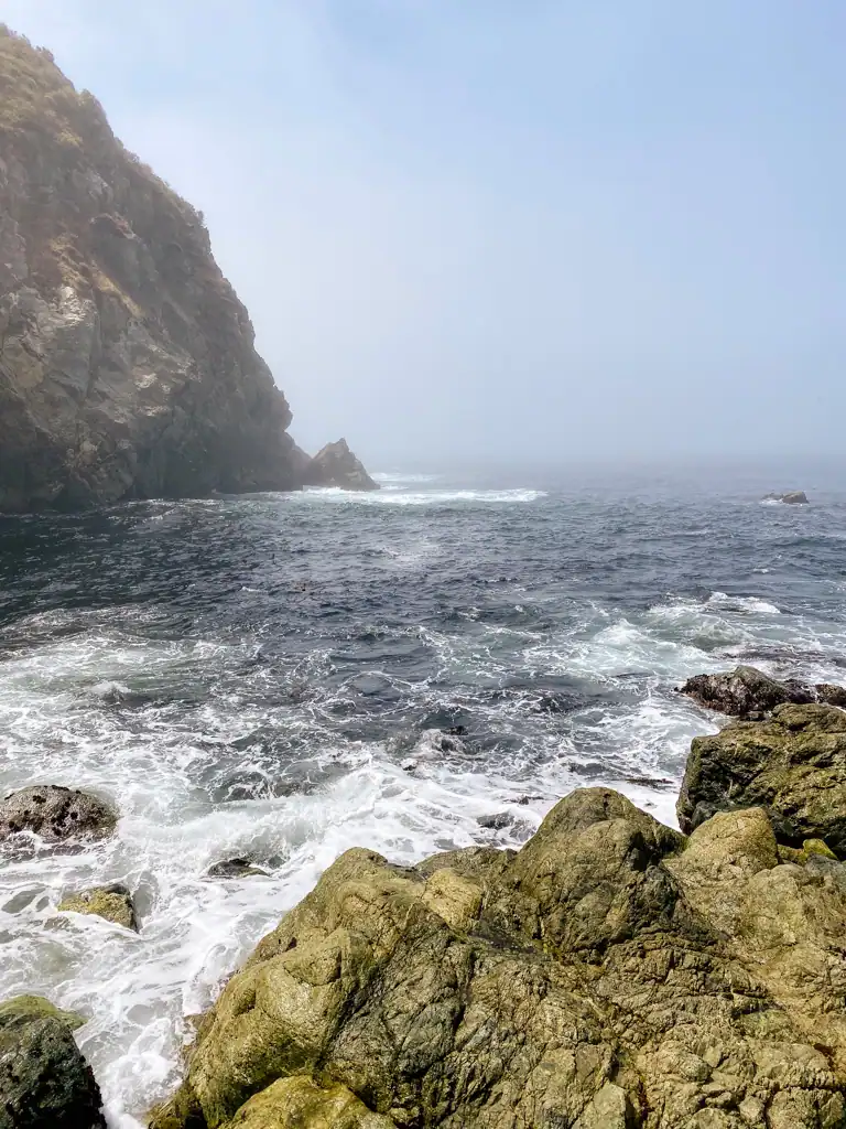A cove view with rocks, fog and the blue ocean. 