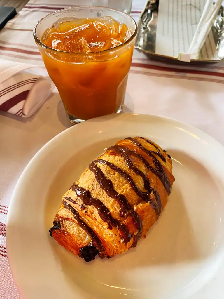 An iced coffee and a pain au chocolate on a plate. 