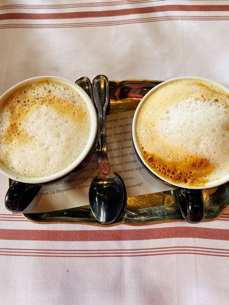 two foamy coffees on a silver tray with spoons. 