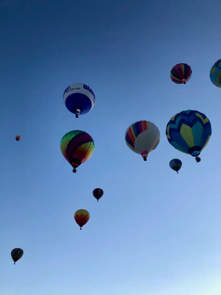 Looking up at many hot air balloons in a blue sky. 