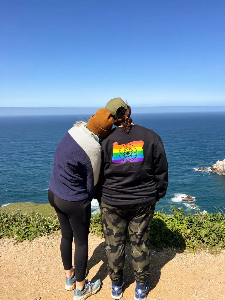 2 women lean on each other while overlooking the ocean on this big sur guide. 