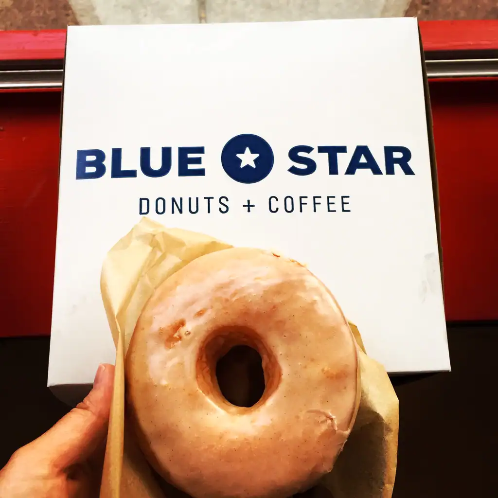 A donut that sits over a white box with blue writing that says "blue star Donut + coffee"