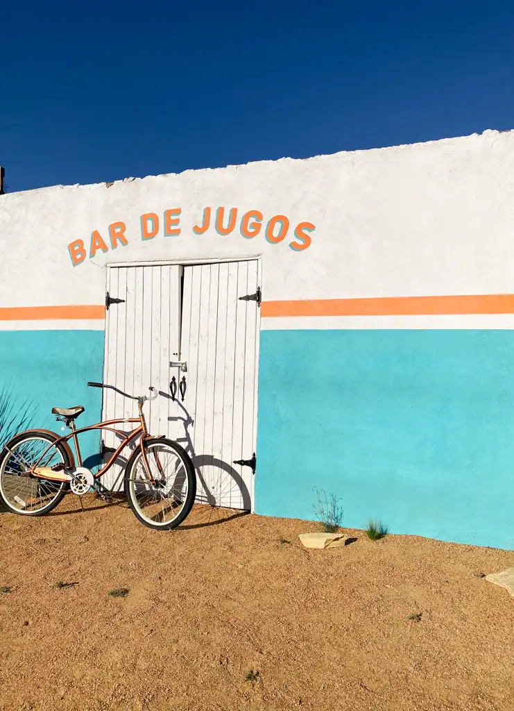 A white and blue building with an orange stripe that says "Bar de jugos" and a bike sitting outside of it. 