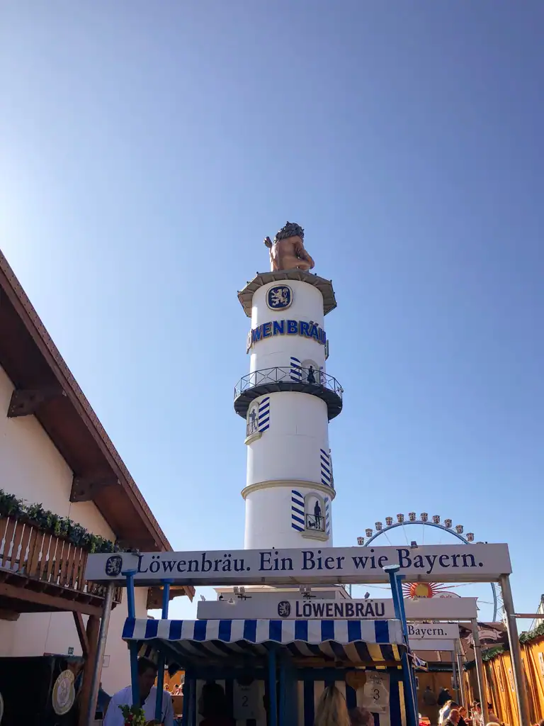 The outside of the Lowenbrau tent at oktoberfest with a large white and blue tower via essential oktoberfest guide. 