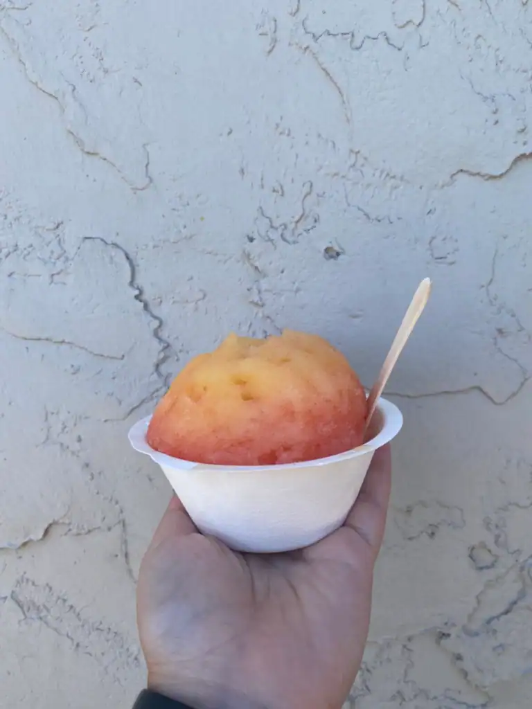 pink and yellow shaved ice held by a hand holding a white cup. 