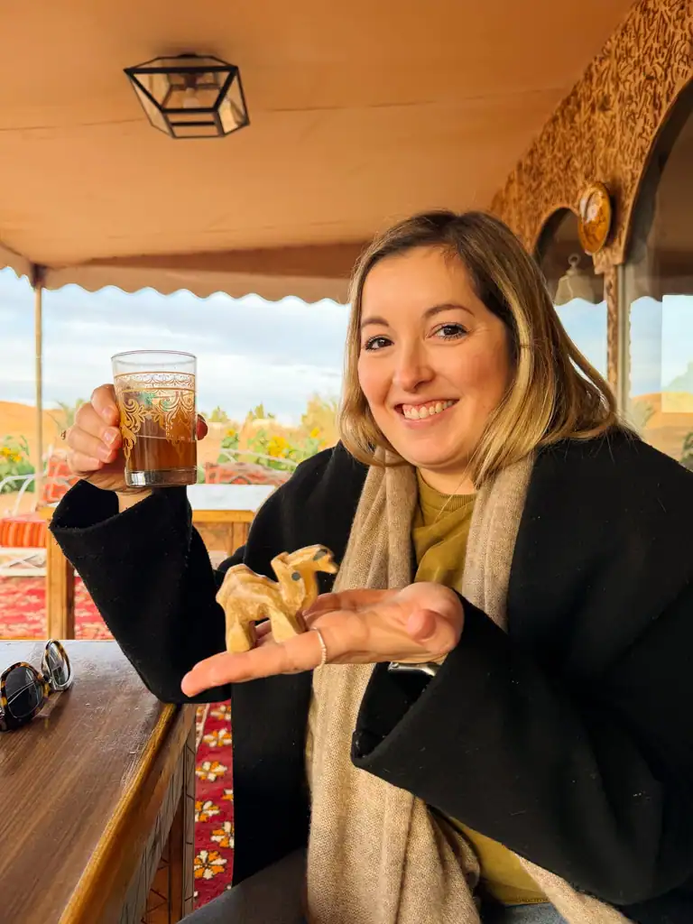 A girl in a black coat holds a small camel figurine and a glass of mint tea in morocco.