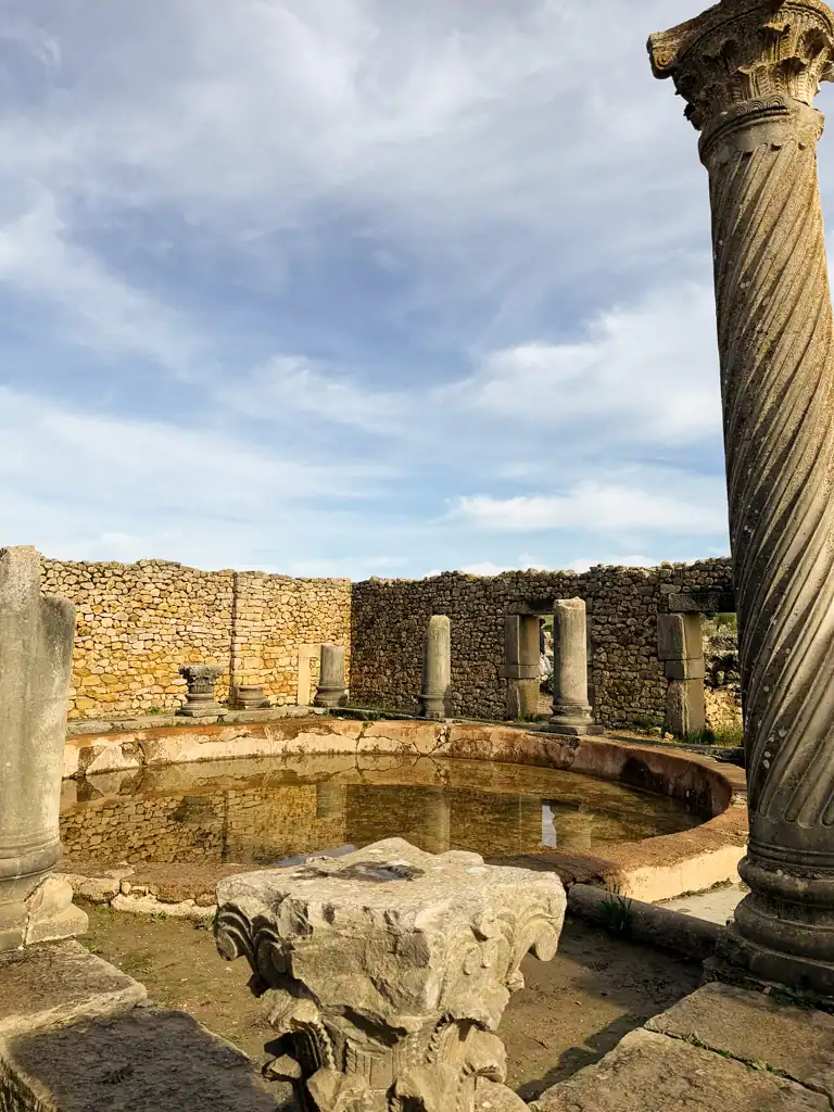 A large pool with broken roman columns surrounded by a brick wall in Volubilis. 