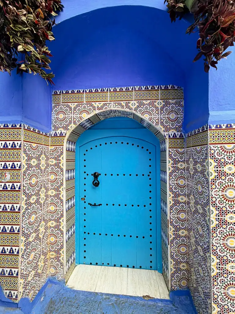 A bright blue door sits between intricate mosaics on either side with blue walls surrounding the top.
