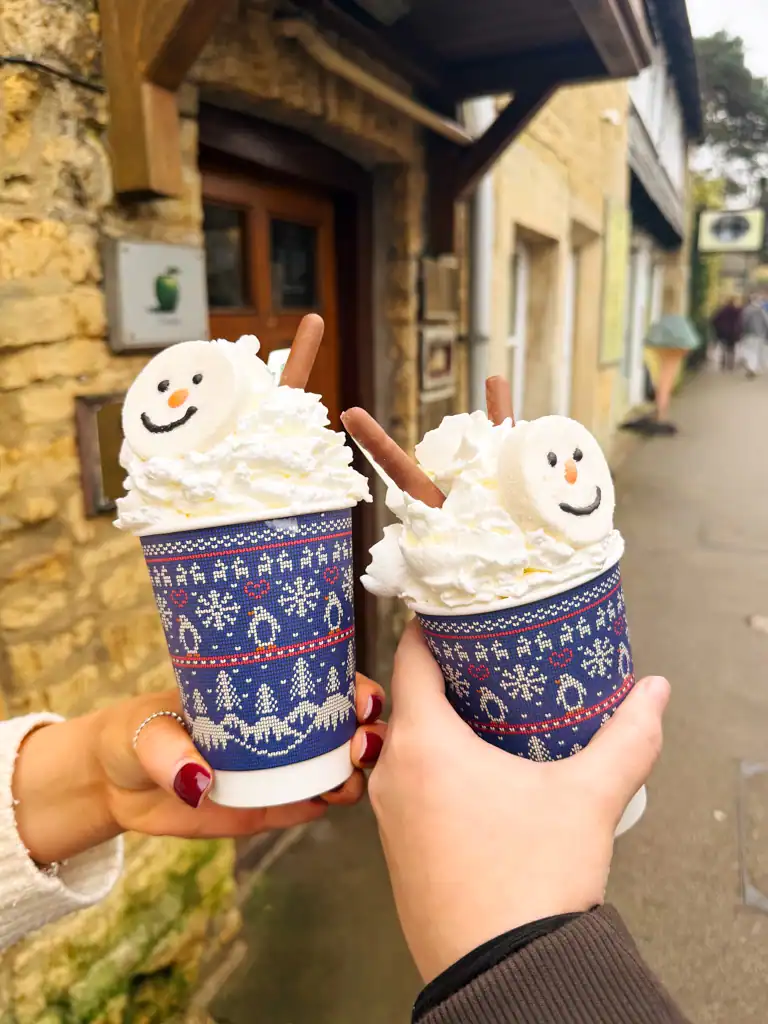two winter hot chocolates with whip cream and a snow man face cookie. 
