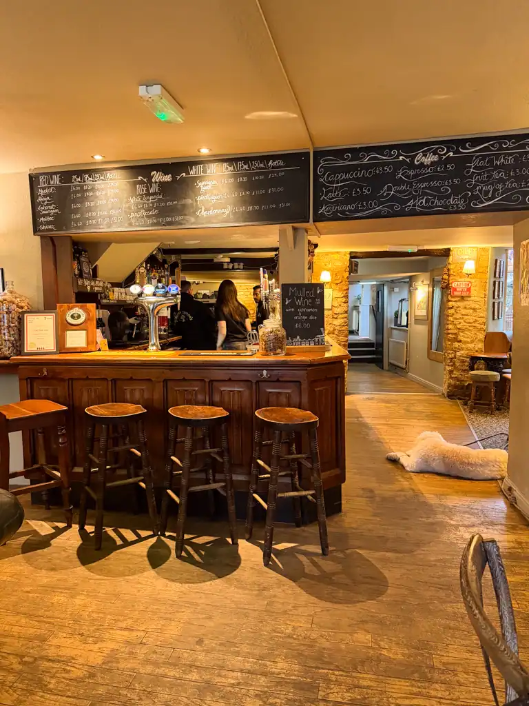 A bar with a large chalkboard menu, stools and bit white dog. 
