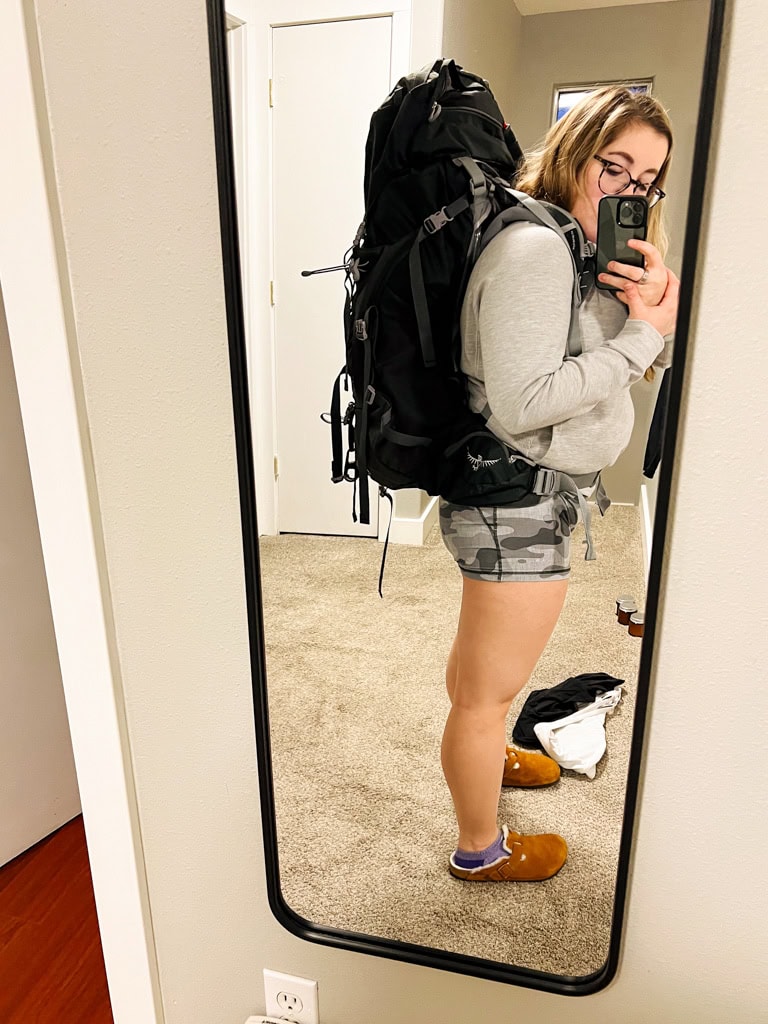 a girl looking in a mirror with her backpacking backpack on. 