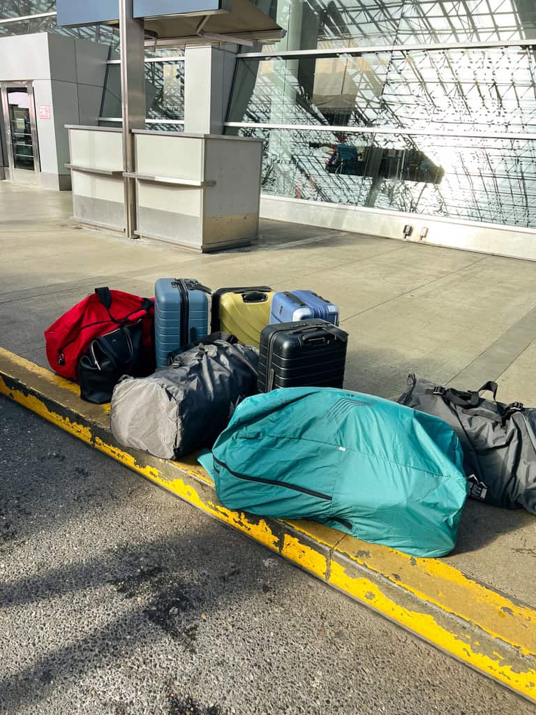 a pile of bags and suitcases outside of the airport. 