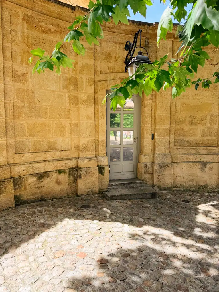 a cobblestoned courtyard with golden stone, a tree and historic looking hanging lamp. 
