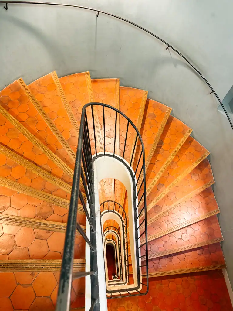 a stairwell in aix-en-provence with red stone stairs and a iron banister. 