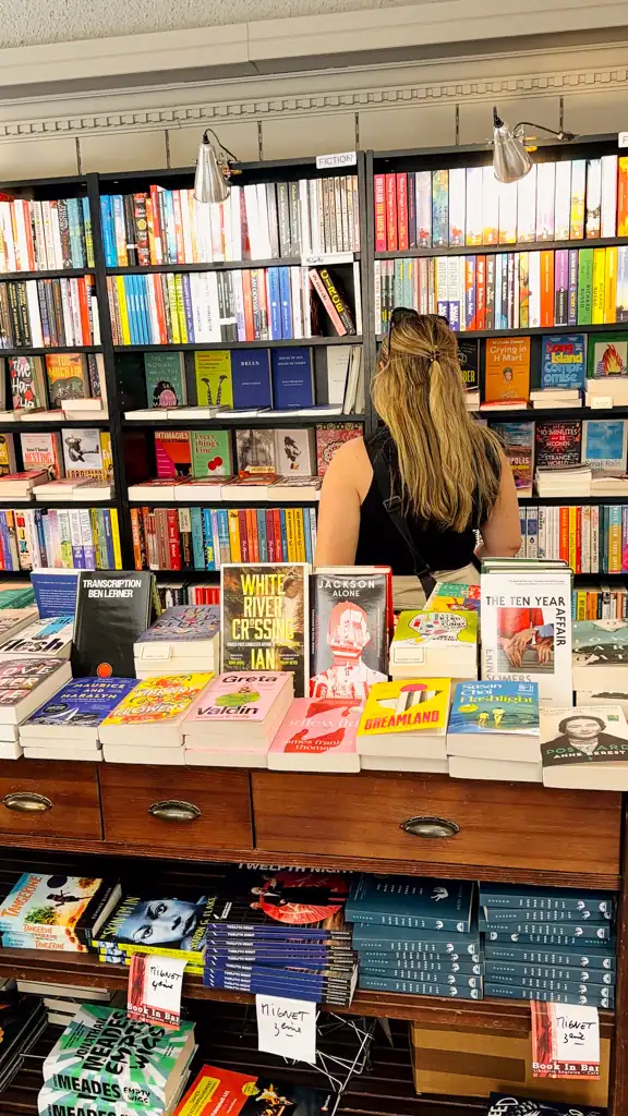a woman with long hair stands in between stacks of books in a book store. 